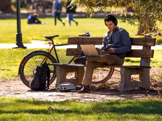 Man sitting on park bench wearing headphones with a laptop on his lap