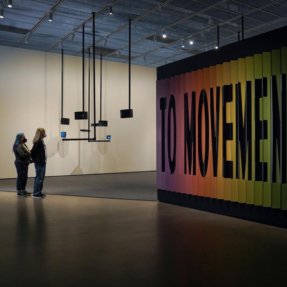 To visitors admire a large peice of art that says MOVEMENT