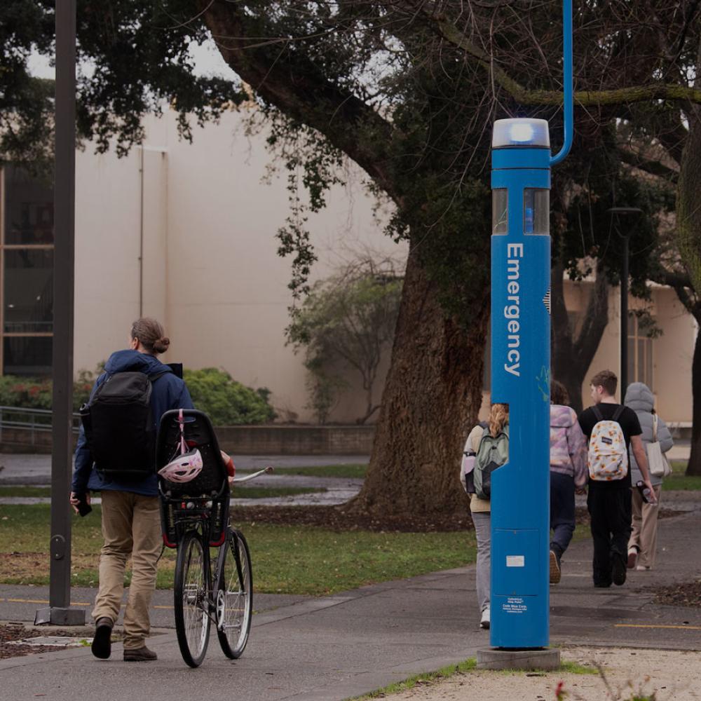 A student walking their bike past an emergency callbox on the UC Davis campus
