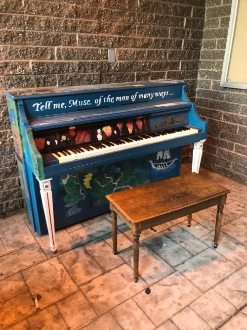 A piano placed outside the local library with "Tell me, Muse, of the man of many ways" from The Odyssey painted on it.