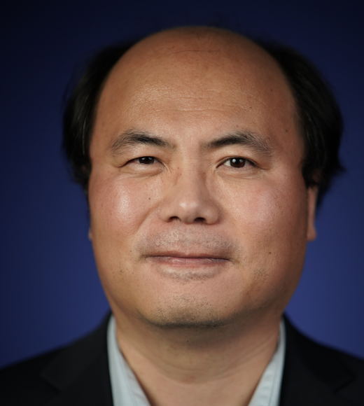 A person wearing a dark blazer and light shirt on a dark blue background.