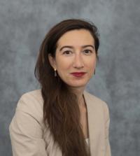 a woman with long hair running down the right side of her chest, stares at the camera during a professional photo shoot in front of a stock grey background.