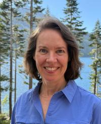 Woman dressed in blue with trees and blue sky behind her