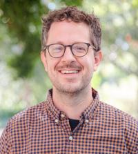 a professional photo of faculty Randy Carney, who is smiling and staring at the camera outside with a blurred tree for background