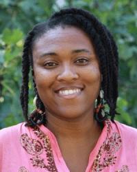 a woman with braids wearing a pink blouse smiles and stares at the camera for a profile picture