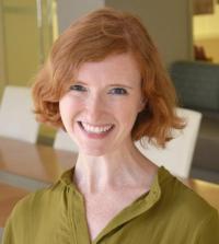 wearing a green blouse and bearing red hair, Lauren Young smiles for the camera inside an office-like indoors setting.