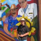 Professor Malaquias Montoya poses in front of his new mural at Beamer Park Elementary School in Woodland.