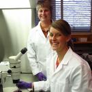 Paula Goines sitting at microscope with Pamela Lein standing behind