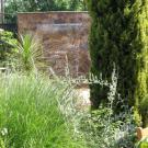 Look beyond the golden Italian cypress tree to see the garden&rsquo;s 10-foot-high rock wall and waterfall.