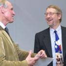 In a photo, two men stand laughing.