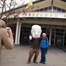 Ryan Bulis wears the Freeborn mask, as Anna Ng takes a Polaroid picture of "Freeborn" and an unidentified passer-by in front of Freeborn's namesake ha