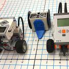 Three small robots, two on wheels, sitting on a paper grid