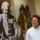 Physics professor Steve Carlip stands next to a bigger-than-life image in the Physics and Geology building of Albert Einstein riding a bike. Theories that Einstein published in 1905 have provided a catalyst for the work of Carlip and several oth