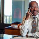 Chancellor Gary S. May at desk, smiling, hand to cheek, no jacket