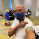 Chancellor Gary S. May, in mask, rolls up sleeve to show bandage over innoculation.