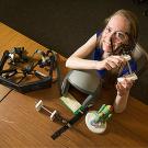 Woman staring through an optical device looking up at the camera, with various devices on the table