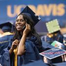 In a sea of other graduates, a female in graduation cap and gown uses her cell phone
