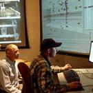 Photo: Three men in room looking at computers and screen