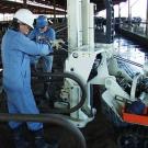 Photo: Two researchers in suits and hard hats work on drilling machine in dairy.