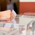 Hand placing ballot into a clear plastic box