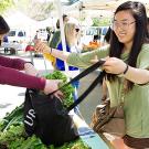 Woman places bunch of leaf lettuce in other woman's cloth shopping bag