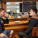 Two students drink beer at a wooden bar.