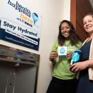 Two women stand next to station for filling water bottles.