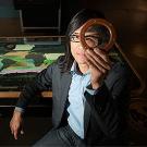 Man sitting at a glass table holding an magnifying circle over his eye
