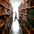 Library stacks, with a patron walking by.