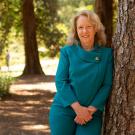 Provost and EVC Mary Croughan leans against tree in Arboretum.
