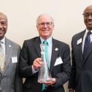 Three men pose for photo, award winner in middle holds decanter award.