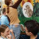 Photo: Woman points at eyes as man watches, another woman paints mural