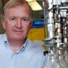 Photo: portrait of man standing next to glass bulbs in lab