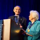 Couple wearing medals hanging from blue ribbons, at UC Davis podium