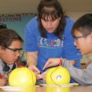 Photo: two young students and a woman examine two grapefruits set up to conduct energy