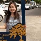 Student holds photo frame while row of cars drives past.