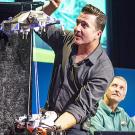 Man demonstrating Mars rover on strings lowering to ground, as another man in background looks on