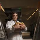 Man in white lab coat holding bowl of bananas stands in laboratory.