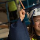 Maria Mu&ntilde;oz in graduation robe and hard hat at a construction site