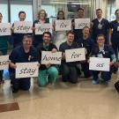 Hospital workers with signs reading "we stay here for you, please stay home for us"