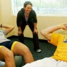 Photo: Woman guiding man doing exercise with another woman with feet in foreground