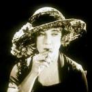 Screenshot from a 1924 film of a woman in a feathered hat smoking a cigarette
