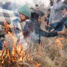Men and women in jackets light field of deergrass on fire as part of cultural burn in California.