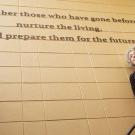 Woman stands in front of sign that reads: Remember those who have gone before...