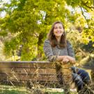 Woman sitting on park bench smiling at camera with lake and trees in background