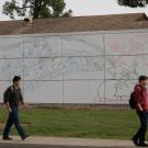 Two students walk past a large, colorful mural on a wall in a grassy area.