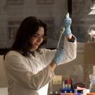 A lab technician uses a pipette, wearing gloves, in a well-lit laboratory.