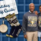a formatted image against an Aggie Blue background designed to look like a Christmas gift features images of holiday merchandise, including bags of coffee and holiday socks. Chancellor Gary S. May and LeShelle May stand next to each other wearing holiday themed UC Davis sweatshirts.