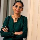 Smiling woman in a green outfit stands with arms crossed against a wall.