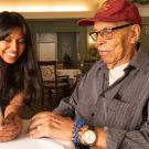 Seated at a table, Avantika Gokulnatha holds a smartphone as she talks with Jack McGruder